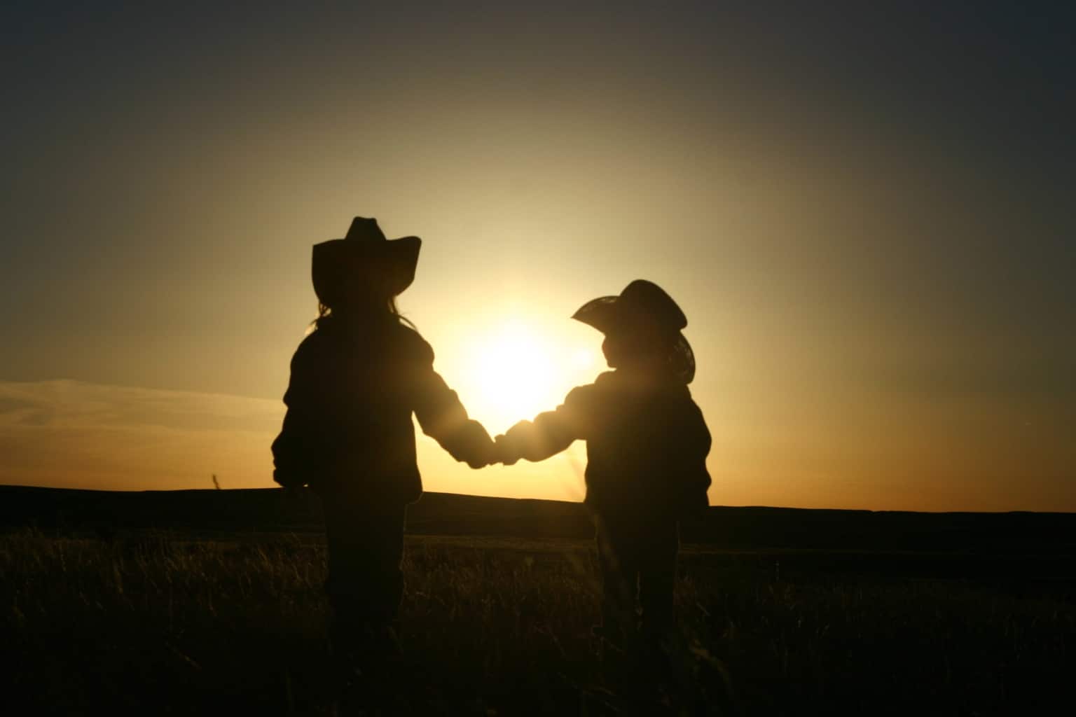 Image of two silhouetted cowgirls holding hands int the sunset