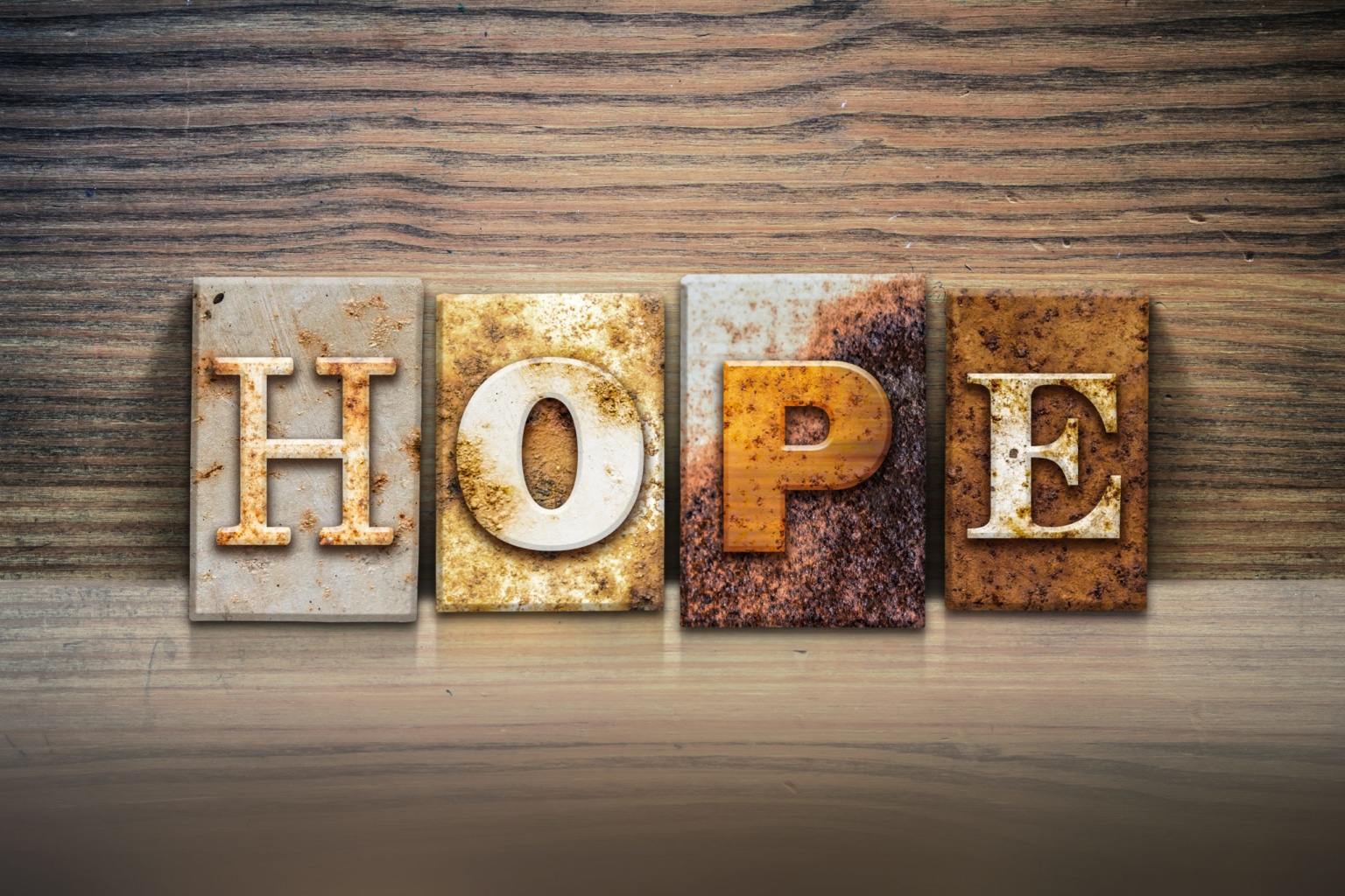The word "HOPE" written in rusty metal letterpress type sitting on a wooden ledge background.